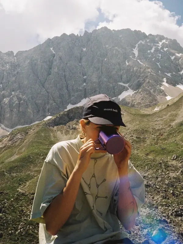 Une randonneuse boit dans sa tasse face aux sommets