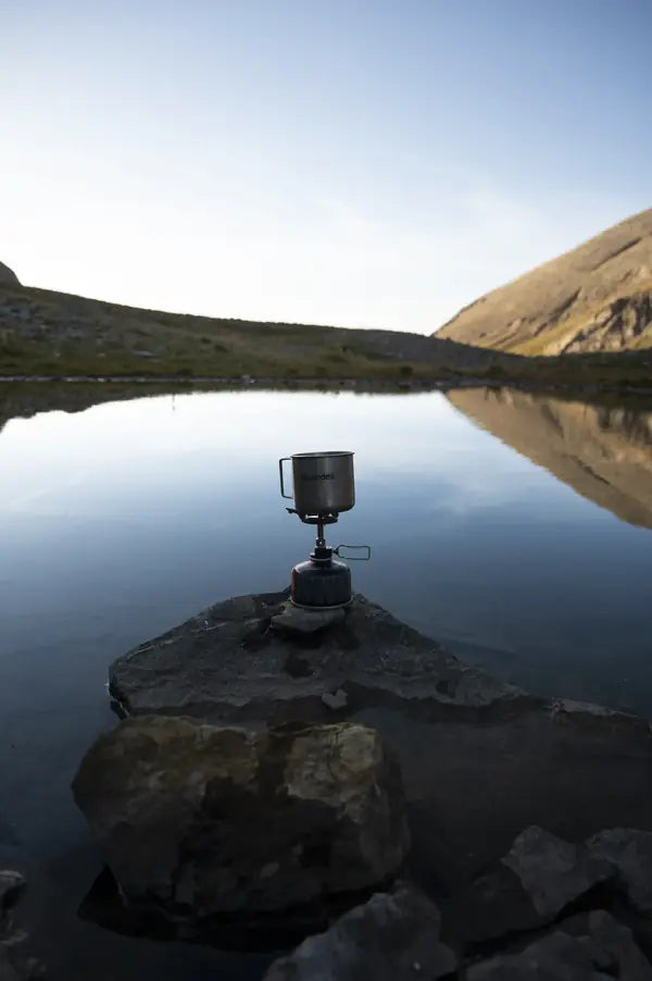 Un réchaud posé sur un rocher au bord d'un lac