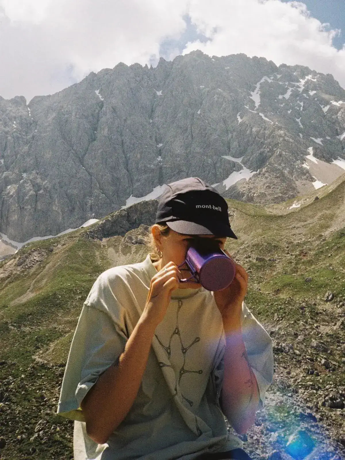 Une randonneuse boit dans sa tasse face aux sommets
